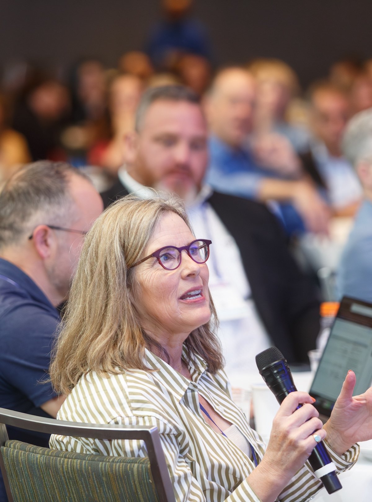 Woman with glasses and a microphone asking questions from the audience